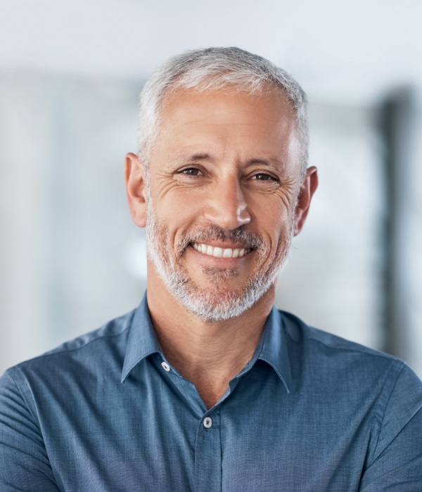 Professional headshot of smiling middle-aged man in blue shirt, dental office setting.