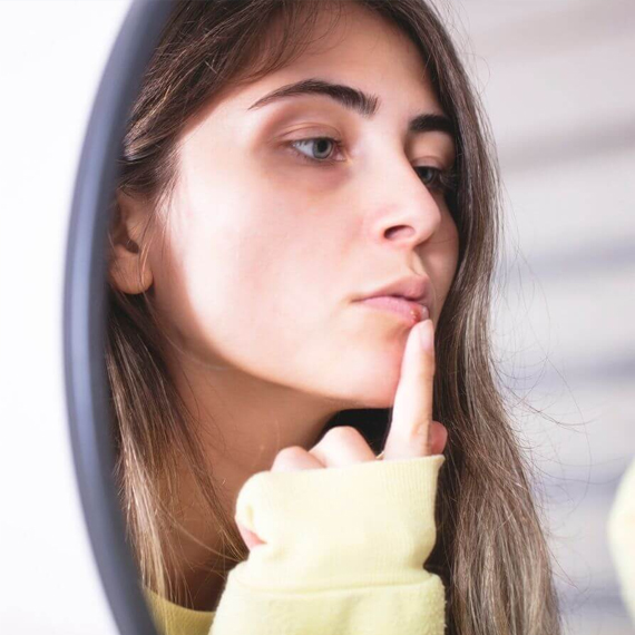 Young woman in thoughtful pose with hand to chin, contemplative expression, neutral background.