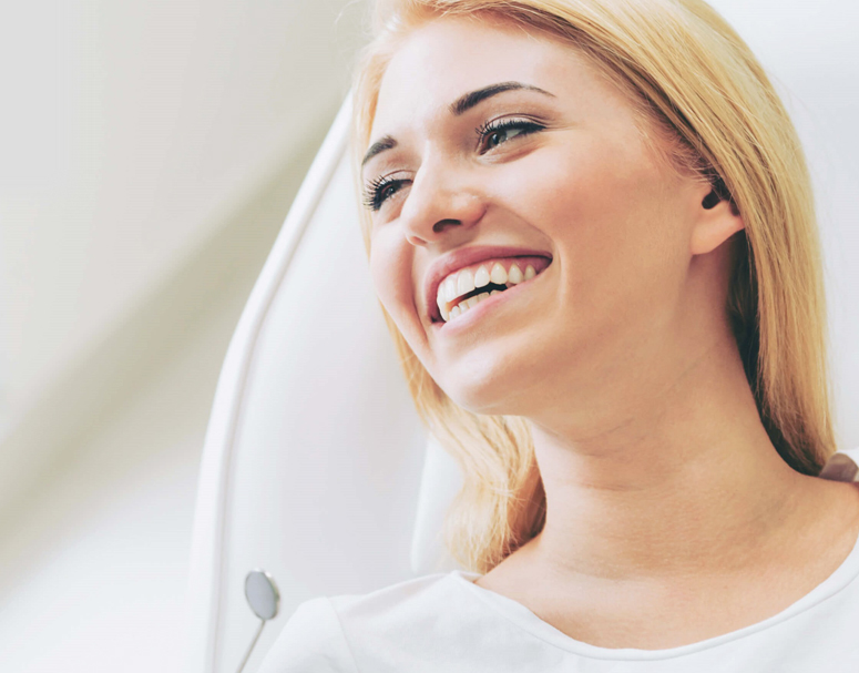 Smiling woman in dental office setting with white background, appearing happy and confident