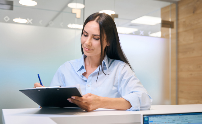 Female dental receptionist holding tablet at front desk in modern dental office