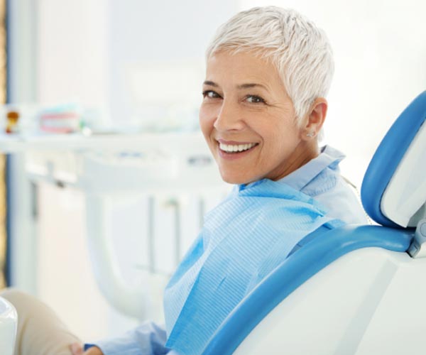 Smiling mature woman in dental chair wearing blue bib at dental office