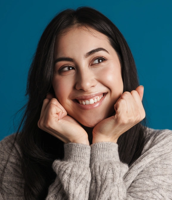 Young woman smiling with hands on face against blue background, dental office portrait