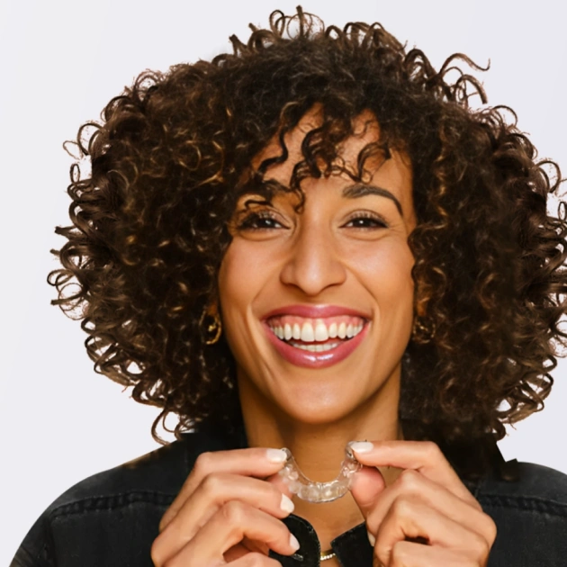 Smiling woman with curly dark hair wearing jewelry against white background for dental practice.