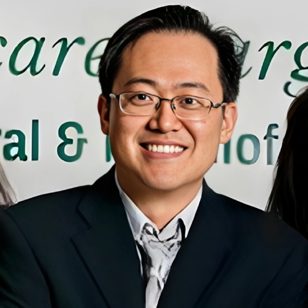 Asian man wearing glasses and dark blazer smiling at dental office event
