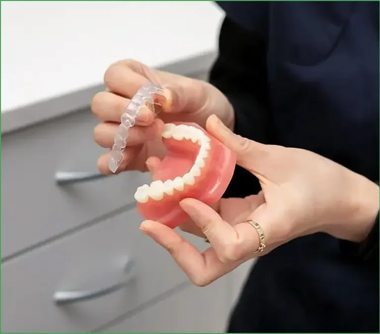 Dentist holding dental prosthetic model demonstrating dentures or dental work in clinical setting.